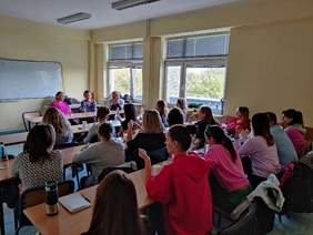 Pokaż zdjęcie: Grupa osób siedzi w sali wykładowej, przodem do tablicy, słucha wykładu